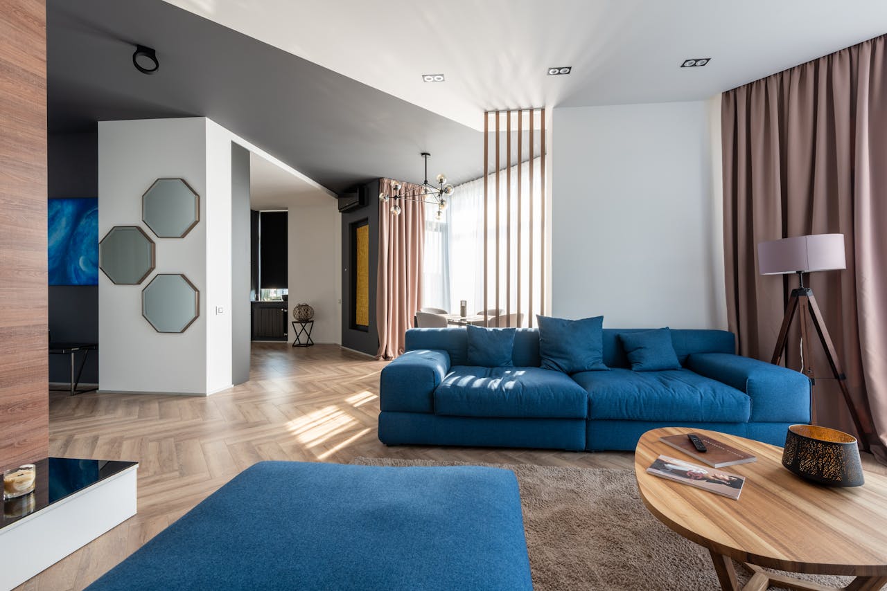 Interior of spacious flat with blue sofa and pouf near wooden table placed on carpet near wall with stylish decorations